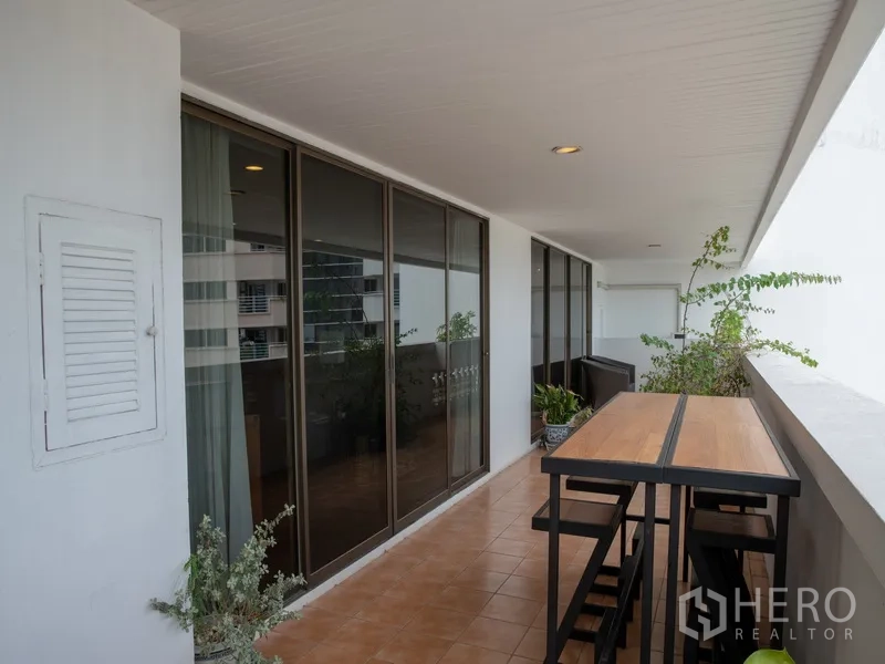 อพาร์ทเมนท์ for rent in Khlong Toei, Bangkok - ระเบียงยาวพร้อมชุดโต๊ะสูงและเก้าอี้ มองสู่ประตูกระจกบานเลื่อน.