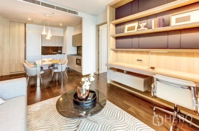 Condominium for rent or sale in Watthana, Bangkok - Living area with built-in shelves and work desk facing the dining and kitchen, set on warm hardwood floors.