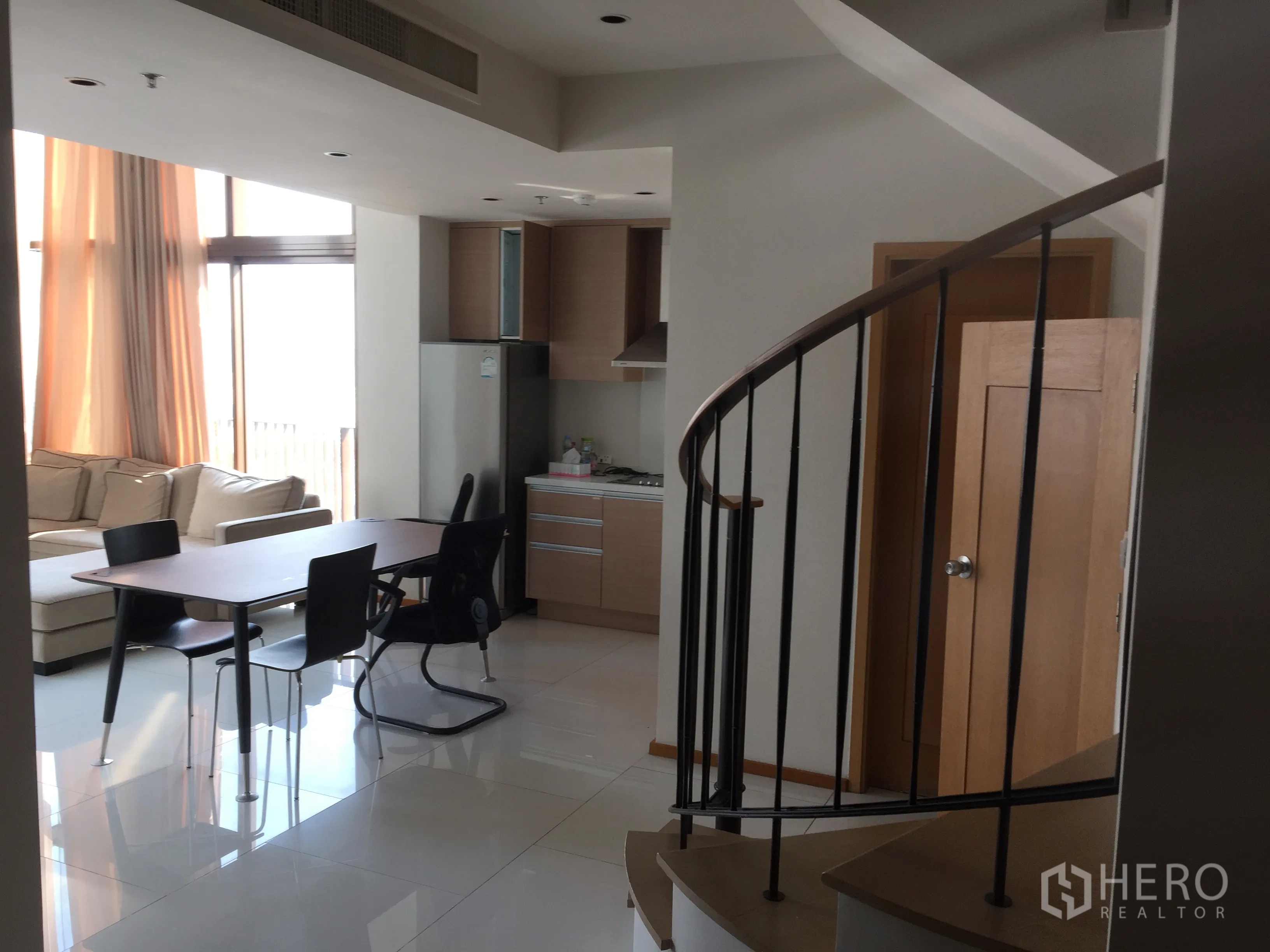 Condominium for rent or sale in Khlong Toei, Bangkok - Open-plan living and dining area with spiral staircase, kitchenette and large windows.