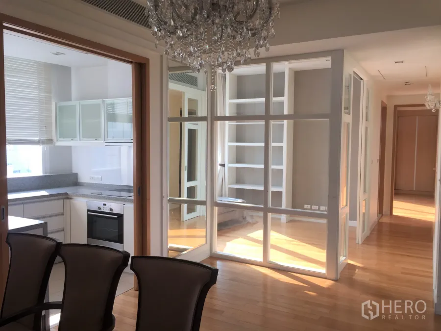 Condominium for rent in Khlong Toei, Bangkok - Bright dining area with chandelier, glass-partitioned study, and view into the closed kitchen over wood floors.