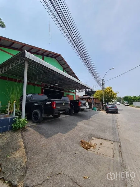 คลังสินค้า ขายในMueang Samut Prakan, Samut Prakan - มุมมองริมถนนของโกดังสีเขียว มีหลังคาเมทัลชีทสำหรับจอดรถและรถกระบะจอดอยู่ ในปากน้ำ สมุทรปราการ