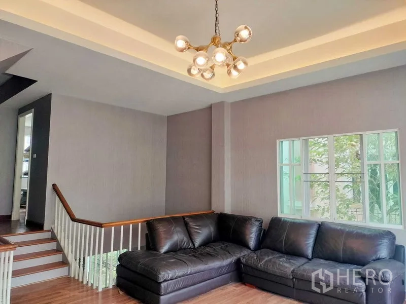 Townhouse for rent in Bueng Kum, Bangkok - Split-level living room with a black L-shaped sofa, tray ceiling and modern chandelier.