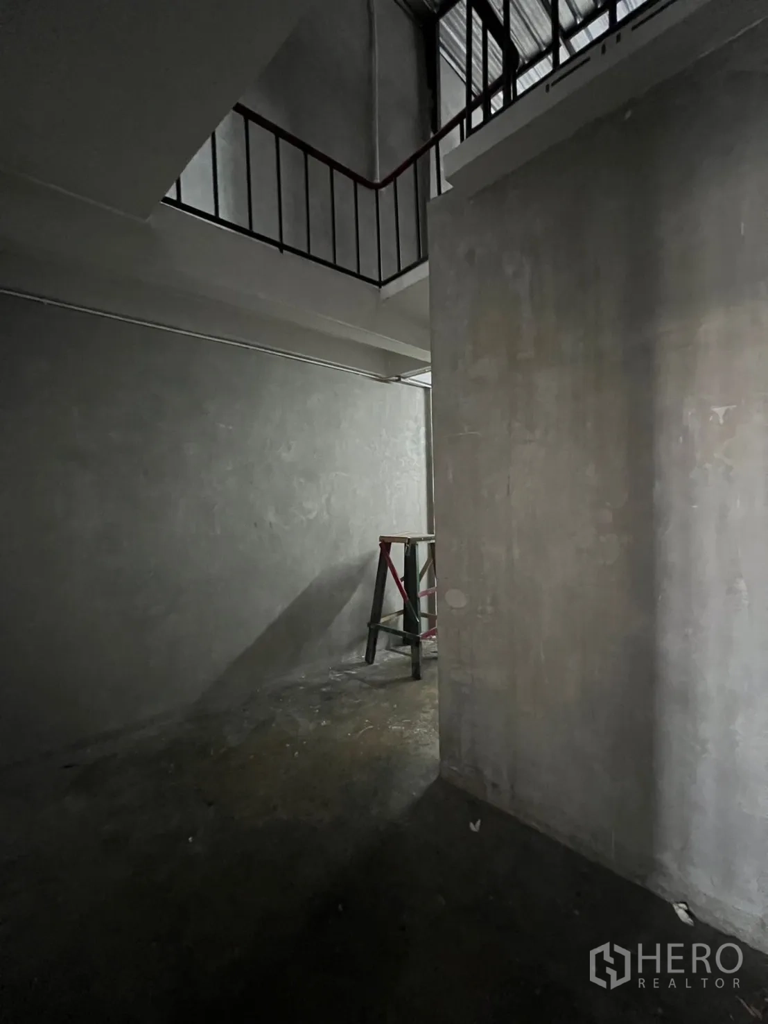 Shophouse for rent in Watthana, Bangkok - Double-height rear area with mezzanine railing and unfinished walls.
