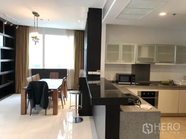 Condominium for rent in Khlong Toei, Bangkok - Modern kitchen with long granite counter, bar seating, and dining area by large windows.