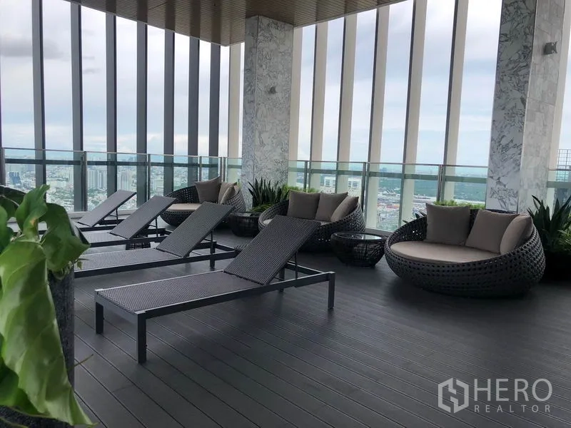 Condominium for rent in Khlong Toei, Bangkok - Sky lounge deck with sun loungers and round daybeds overlooking the city.