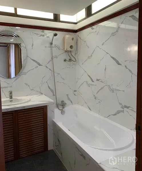 Condominium for rent or sale in Watthana, Bangkok - Bathroom with marble-effect wall tiles, bathtub with shower, and vanity with mirror.