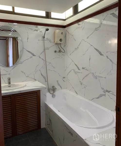 Condominium for rent or sale in Watthana, Bangkok - Bathroom with marble-effect wall tiles, bathtub with shower, and vanity with mirror.