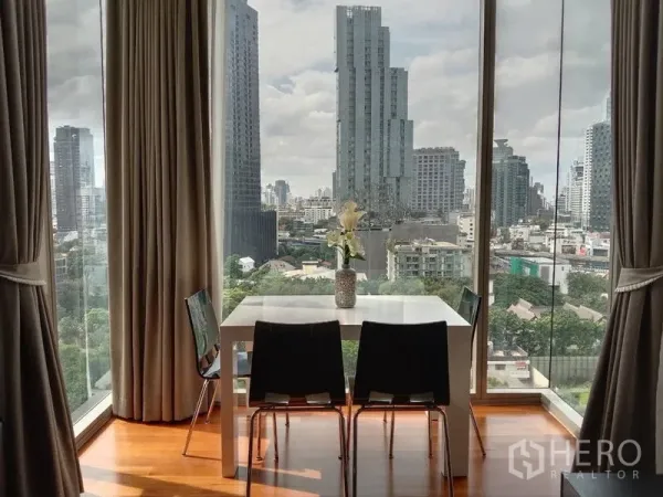 Condominium for rent - Dining table beside floor‑to‑ceiling glass with panoramic Bangkok skyline and wood flooring.