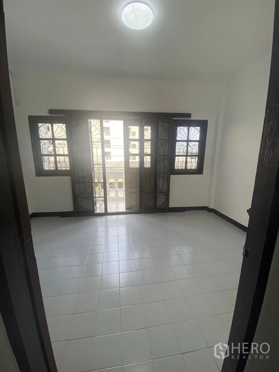Townhouse for rent in Huai Khwang, Bangkok - Bright bedroom with balcony doors, tiled floor, and neighborhood view.