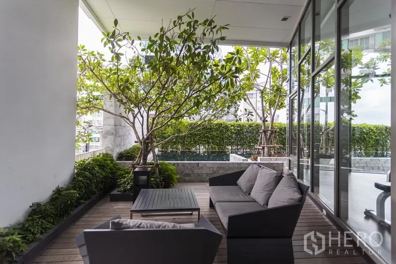 Condominium for rent in Watthana, Bangkok - Shaded outdoor lounge with sofa seating, wooden deck and lush greenery.