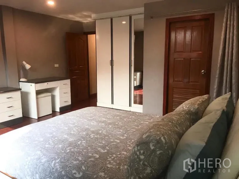 联排别墅 出租在Bang Rak, Bangkok - 卧室配大床、白色衣柜、书桌与木门，灯光温暖。