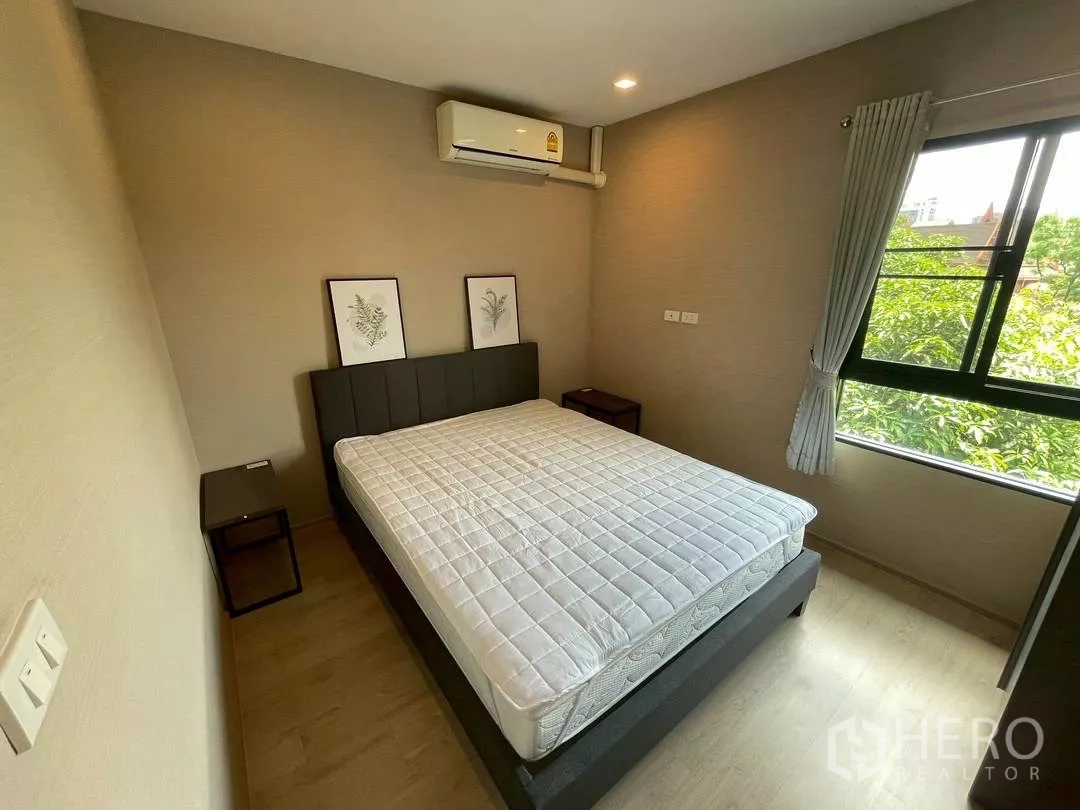 Townhouse for rent in Suan Luang, Bangkok - Bright bedroom with large window, air conditioner and framed botanical art above bedside tables.