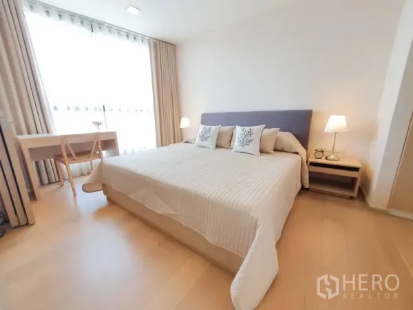 Condominium for rent in Watthana, Bangkok - Serene bedroom with a king-size bed, bedside lamps and a work desk by a floor-to-ceiling window.