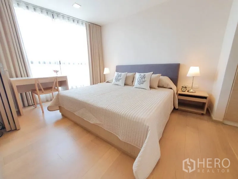 Condominium for rent in Watthana, Bangkok - Serene bedroom with a king-size bed, bedside lamps and a work desk by a floor-to-ceiling window.