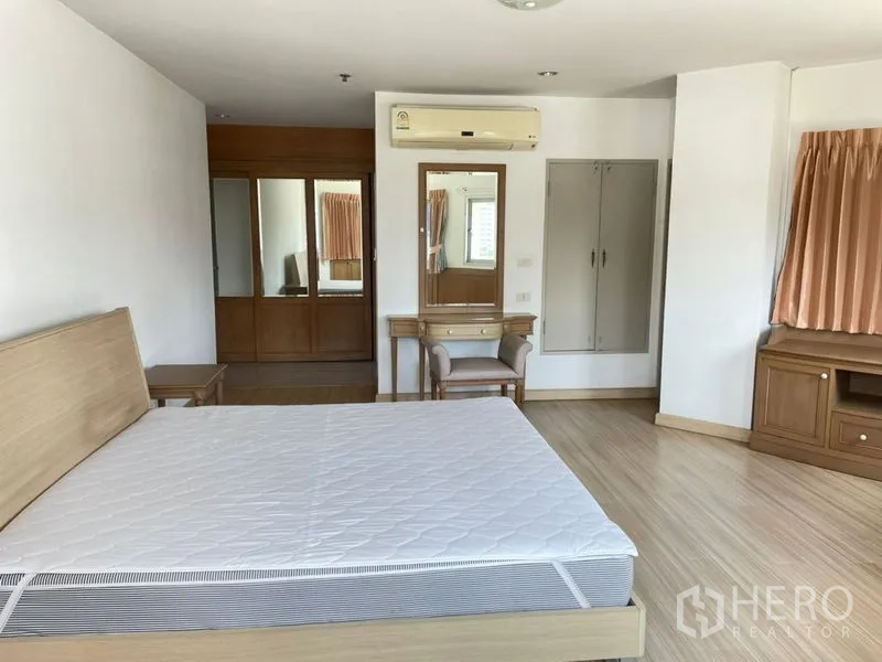 Condominium for rent in Khlong Toei, Bangkok - Master bedroom showing dressing table, mirrored wardrobe, and wood-style flooring.