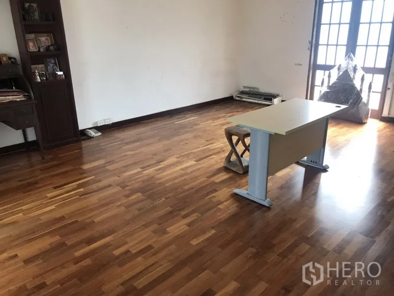 Home Office for rent in Khlong Toei, Bangkok - Spacious room with polished wooden flooring, a simple desk and French doors bringing in natural light.