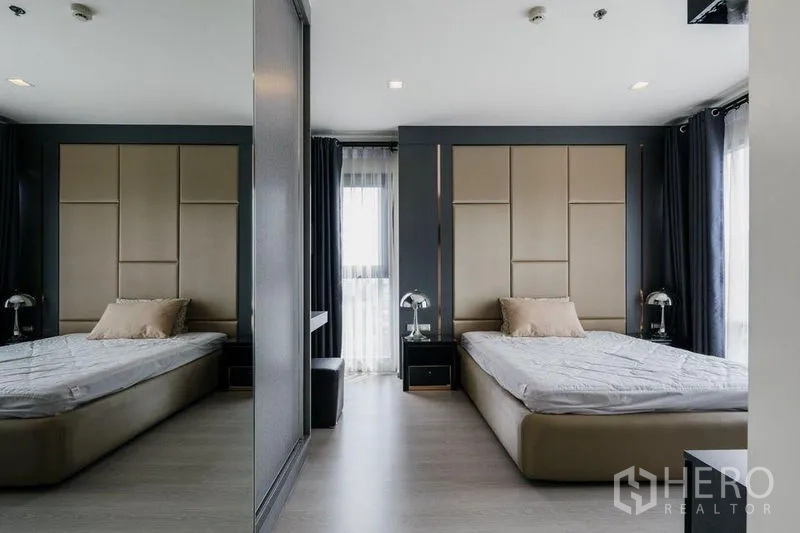 Condominium for rent in Khlong Toei, Bangkok - Second bedroom with padded headboard, mirrored wall, bedside tables, and large windows.