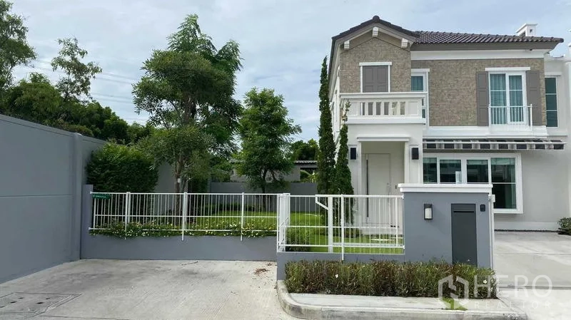 Detached House for rent or sale in Prawet, Bangkok - Two-storey detached house exterior with white fence, driveway and landscaped corner garden in Prawet, Bangkok.