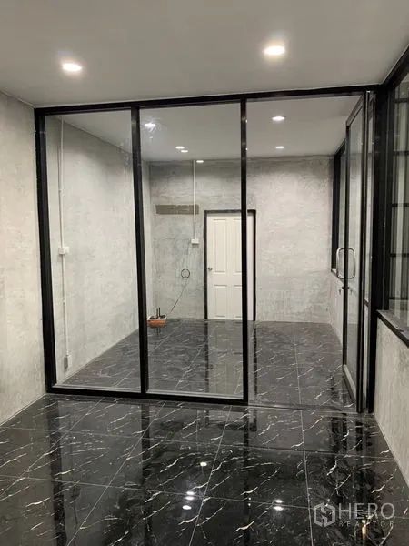 Warehouse for rent in Khan Na Yao, Bangkok - Modern glass-walled office inside the warehouse with black marble-look tiles and recessed ceiling lights.