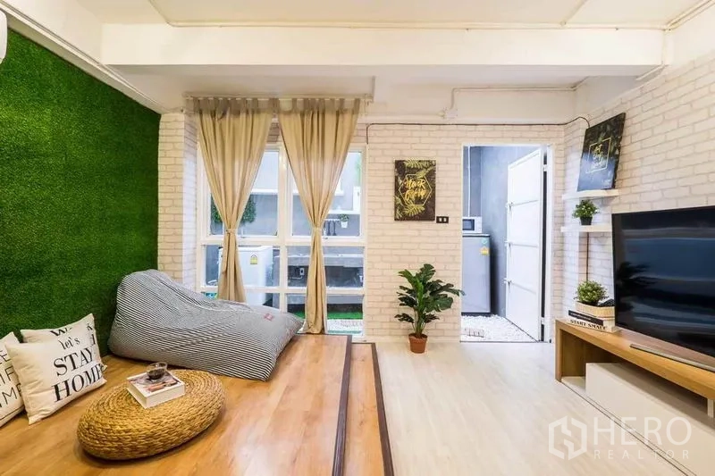 Detached House for rent in Khlong Toei, Bangkok - Cozy living area with raised wooden platform, artificial grass feature wall and TV unit.