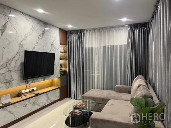 独立式住宅 出租或出售在Lat Krabang, Bangkok - 客厅配大理石纹电视墙、L形沙发、纱帘与筒灯。