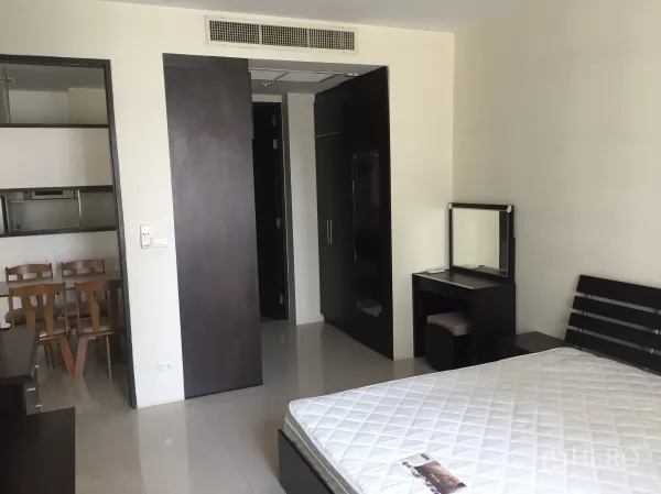Condominium for rent in Khlong Toei, Bangkok - Spacious bedroom with bed frame, dressing table and built-in wardrobe.