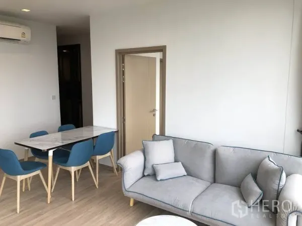 公寓 出租在Watthana, Bangkok - 温馨客厅，灰色沙发与靠垫，旁设紧凑餐桌，极简风格。
