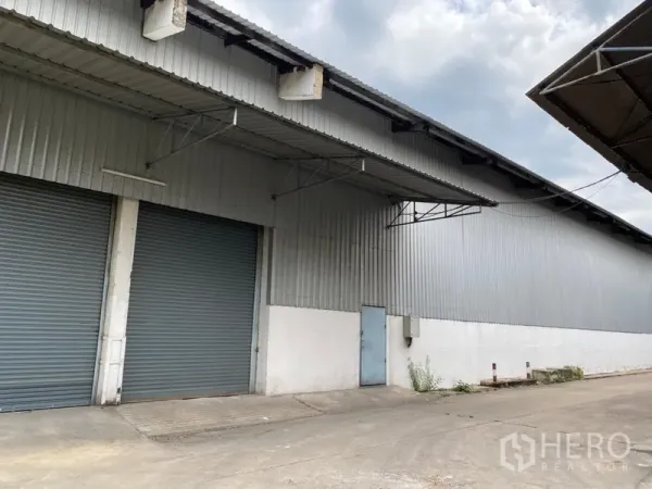 Warehouse for rent in Khlong Luang, Pathum Thani - Metal-clad warehouse exterior with two large roller shutter doors and covered loading canopies.