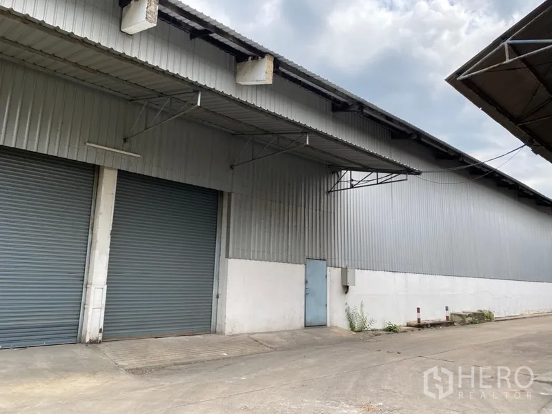 货栈 出租在Khlong Luang, Pathum Thani - 金属板外墙仓库外观，配有两扇大型卷帘门和带顶装卸区。
