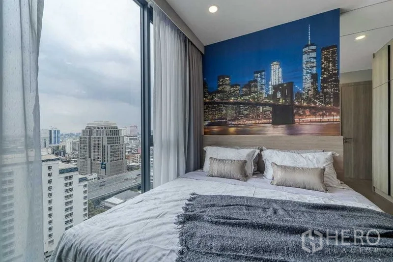 Condominium for rent in Pathum Wan, Bangkok - Corner bedroom with floor-to-ceiling windows, city skyline view and a dramatic cityscape mural behind the bed.