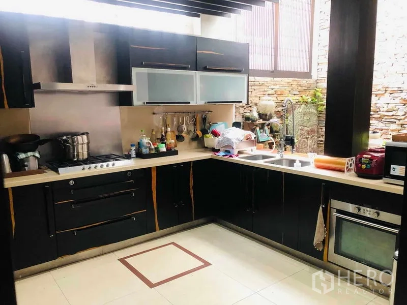 Townhouse for rent in Yan Nawa, Bangkok - Modern L-shaped kitchen featuring black cabinetry, stainless-steel hood, and a stone feature wall.