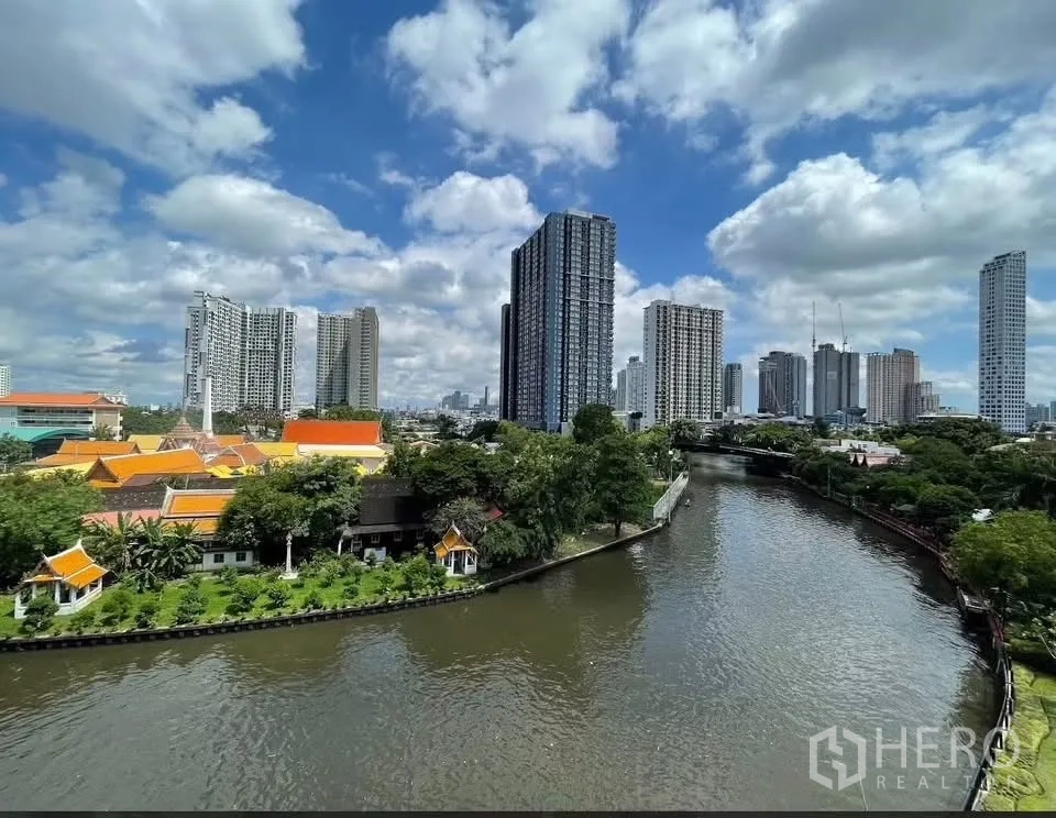 Condominium for rent in Watthana, Bangkok - Panoramic view of a canal curving through the city with high-rise buildings under blue skies.