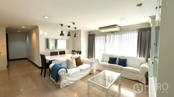 Condominium for rent or sale in Watthana, Bangkok - Living room with two white sofas, floor-to-ceiling curtains, and adjacent dining set.