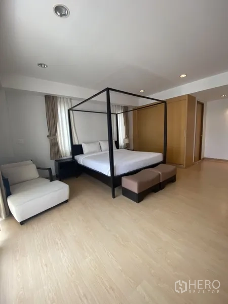 房间 出租在Watthana, Bangkok - 主卧配四柱床、休闲椅与内置衣柜，木地板。