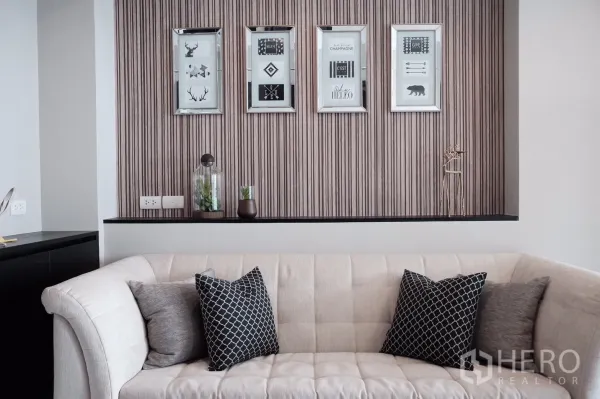 Condominium for rent or sale in Khlong Toei, Bangkok - Contemporary living room with a cream sofa, patterned cushions and framed wall art on a textured feature wall.