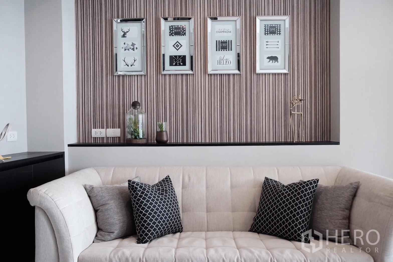 Condominium for rent or sale in Khlong Toei, Bangkok - Contemporary living room with a cream sofa, patterned cushions and framed wall art on a textured feature wall.