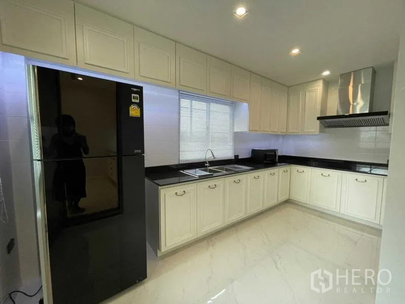 独立式住宅 出租或出售在Lat Krabang, Bangkok - 现代L形厨房，奶油色橱柜，黑色台面，不锈钢油烟机与大冰箱。
