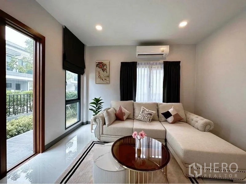 独立式住宅 出租或出售在Bang Phli, Samut Prakan - 通透客厅，L形沙发、圆形茶几与大窗。