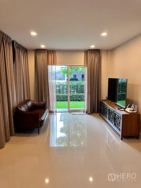 独立式住宅 出售在Prawet, Bangkok - 面向花园的起居室，配沙发、电视与落地推拉门。