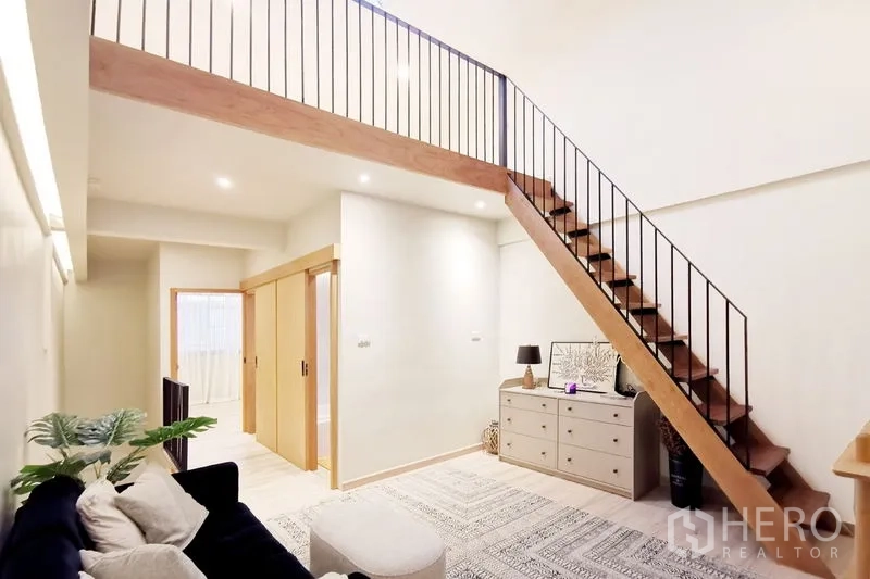 Townhouse for rent in Khlong Toei, Bangkok - Loft-style lounge with timber stairs, sliding doors to rooms and a sideboard unit.