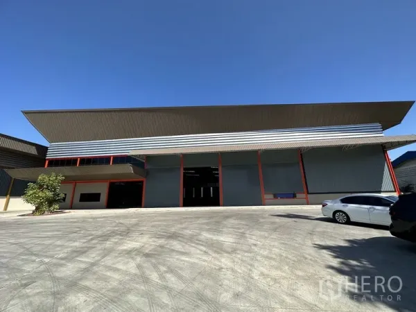 工厂 出租在Chachoengsao - 现代工厂外立面，高挑屋顶、多个卷帘门与宽阔混凝土场地，天空晴朗