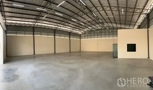 Warehouse for rent in Bang Bo, Samut Prakan - Spacious warehouse interior with high steel truss roof, polished concrete floor, ventilation panels and an enclosed office box.
