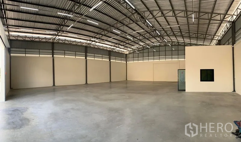 Warehouse for rent in Bang Bo, Samut Prakan - Spacious warehouse interior with high steel truss roof, polished concrete floor, ventilation panels and an enclosed office box.