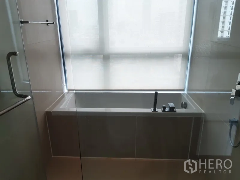 公寓 出租在Watthana, Bangkok - 浴室带浴缸，旁有磨砂窗与玻璃淋浴间。