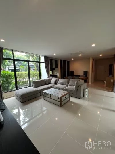 Detached House for rent in Bang Kapi, Bangkok - Bright living room with large sectional sofa, floor-to-ceiling windows and glossy tiled floor facing the garden.