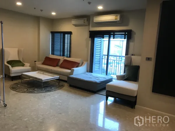 Condominium for rent in Khlong Toei, Bangkok - Spacious living room with sofas, balcony access, marble floors and split air-conditioning.