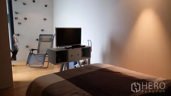 Condominium for rent or sale in Sathon, Bangkok - Cozy bedroom with TV console and lounge chair on light wood flooring.