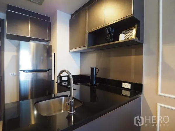 Condominium for rent in Khlong San, Bangkok - Modern kitchen with black stone countertop, sink island, and stainless-steel refrigerator and cabinetry.