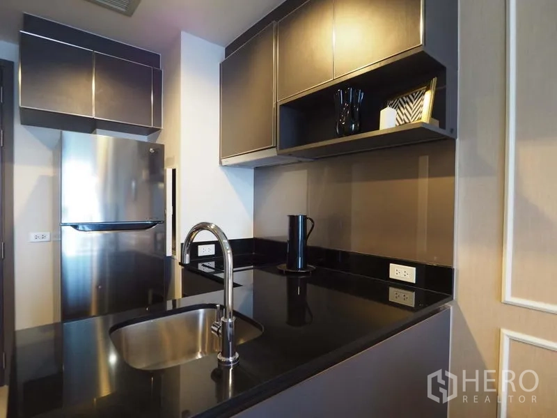 Condominium for rent in Khlong San, Bangkok - Modern kitchen with black stone countertop, sink island, and stainless-steel refrigerator and cabinetry.