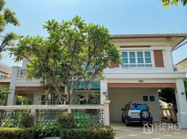 Detached House for rent or sale in Min Buri, Bangkok - Front view of a two-storey detached house in Min Buri with mature tree, front garden, gated fence and covered carport.
